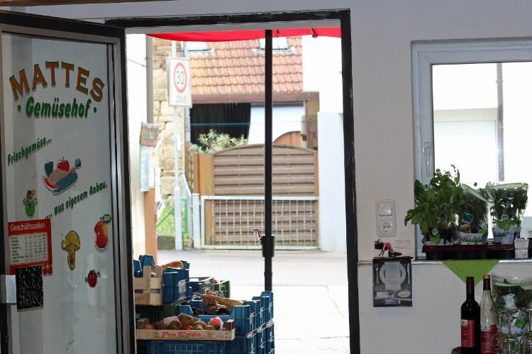 Eingang zu einem Gemüsehof mit Schild "MATTES Gemüsehof" und Kisten mit Gemüse im Vordergrund.