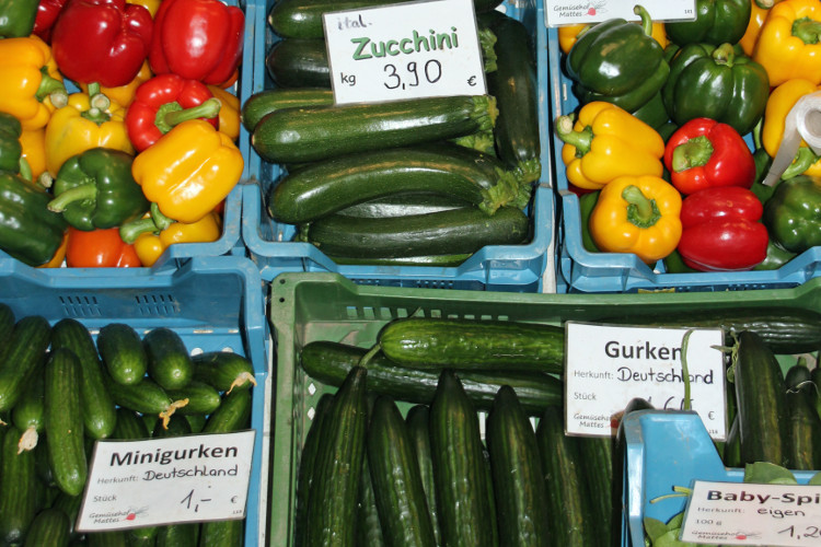 Farbenfrohe Gemüse-Angebot mit Zucchini, Gurken, Minigurken und Paprika in Kisten mit Preisschildern.